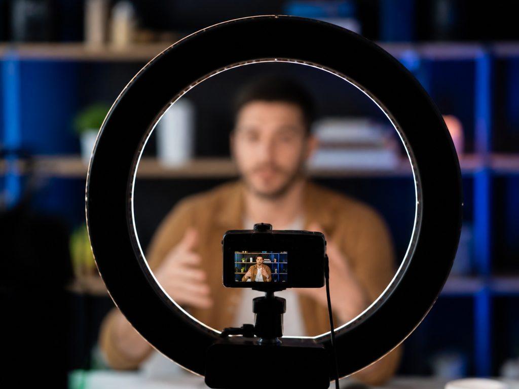 Pessoa gravando conteúdo em frente a uma câmera dentro de um ring light, representando produção profissional sem aparecer todos os dias